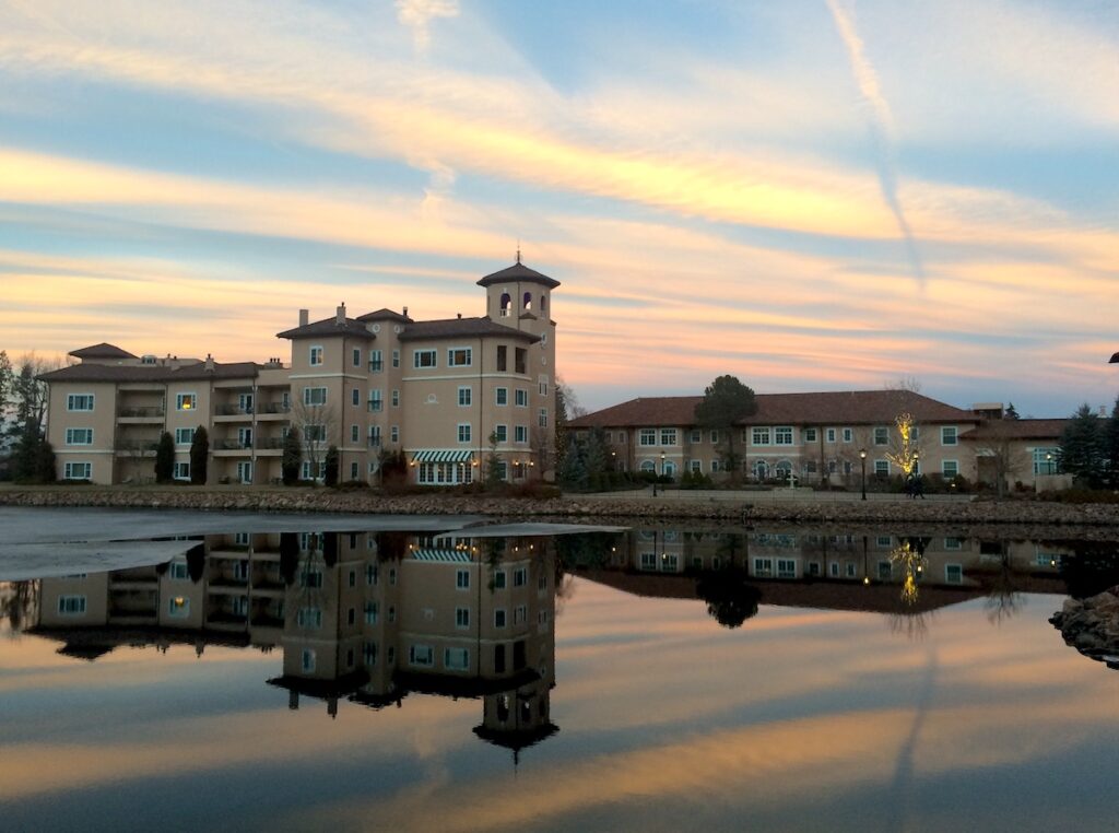 Luxury hotel building against colorful sunset reflecting on pond during winter. The Broadmoor Hotel, Colorado Springs, Colorado.
