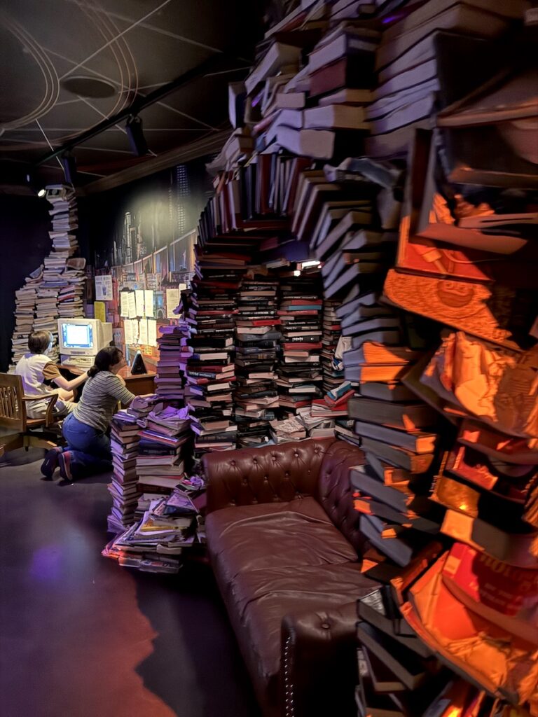 Archway of books and people working on computers in other-worldly interactive art exhibit. Meow Wolf Denver Convergence Station, Denver, Colorado.