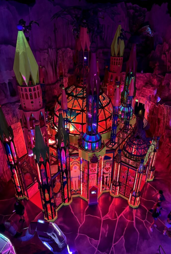 Giant, multi-story castle back lit bright pink in other-worldly interactive art exhibit. Meow Wolf Denver Convergence Station, Denver, Colorado.
