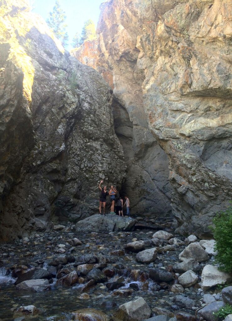 Group of girls hiking in narrow, rocky chasm waving to camera on sunny summer day. Zapata Falls hike near Great Sand Dunes National Park and Alamosa, Colorado.