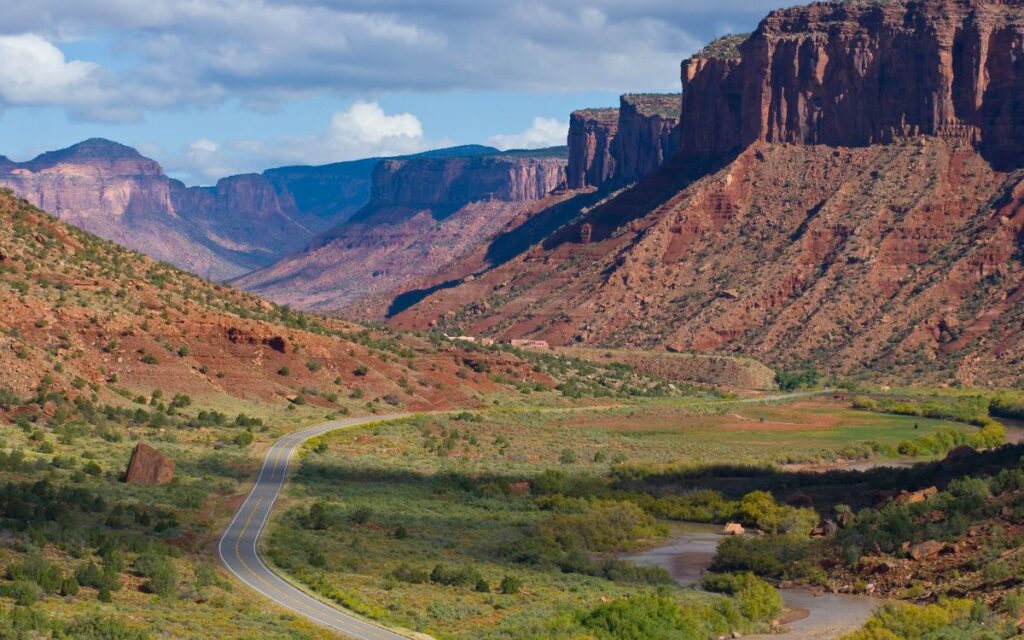 Red rock cliffs and buttes overlooking road and river winding through green valley. Dolores River, Gateway, Colorado.