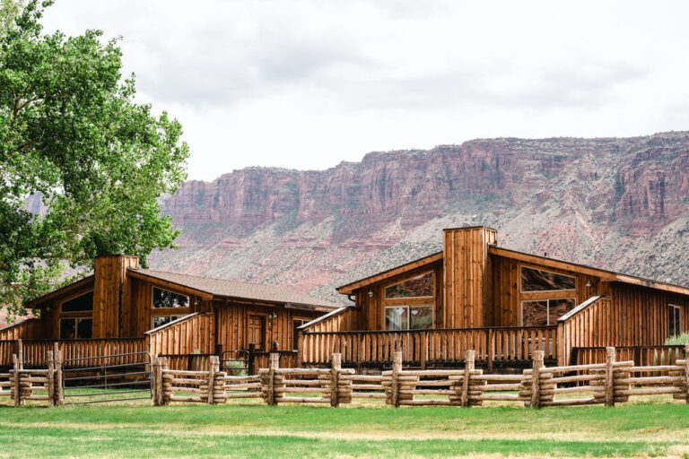 Two log cabins with red rock cliff background on sunny day. Red Cliffs Lodge Hotel, Moab, Utah.