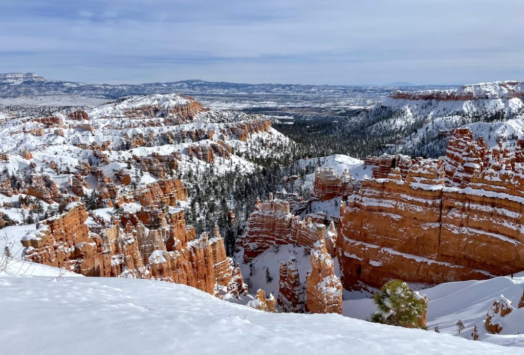 Red rock canyon covered in snow with mountain views in distance on sunny summer day. Sunrise Point, Bryce Canyon National Park, Utah.