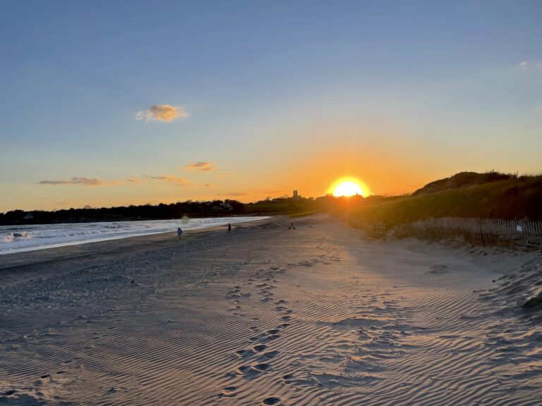 Golden sandy beach at sunset with waves crashing the shore and people in distance. Second Beach, Newport, Rhode Island.