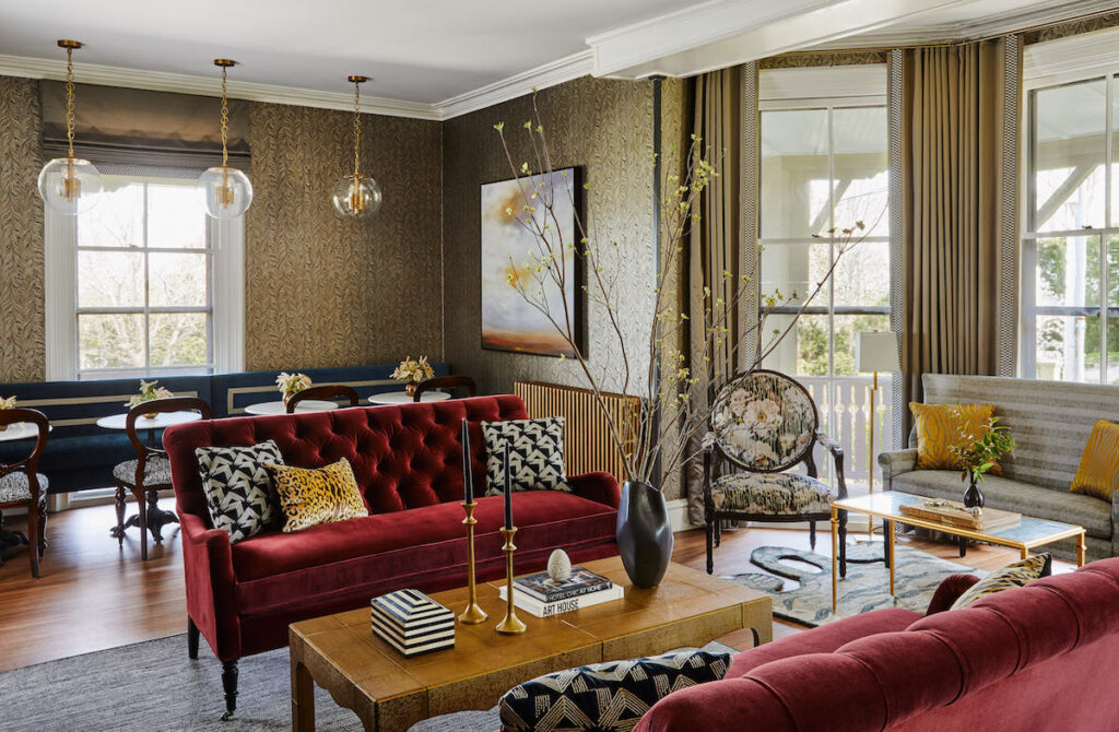 Hotel guest seating area with plush velvet couches, small dining area, and large bay windows in well renovated historic Victorian mansion. Cliffside Inn hotel, Newport, Rhode Island.