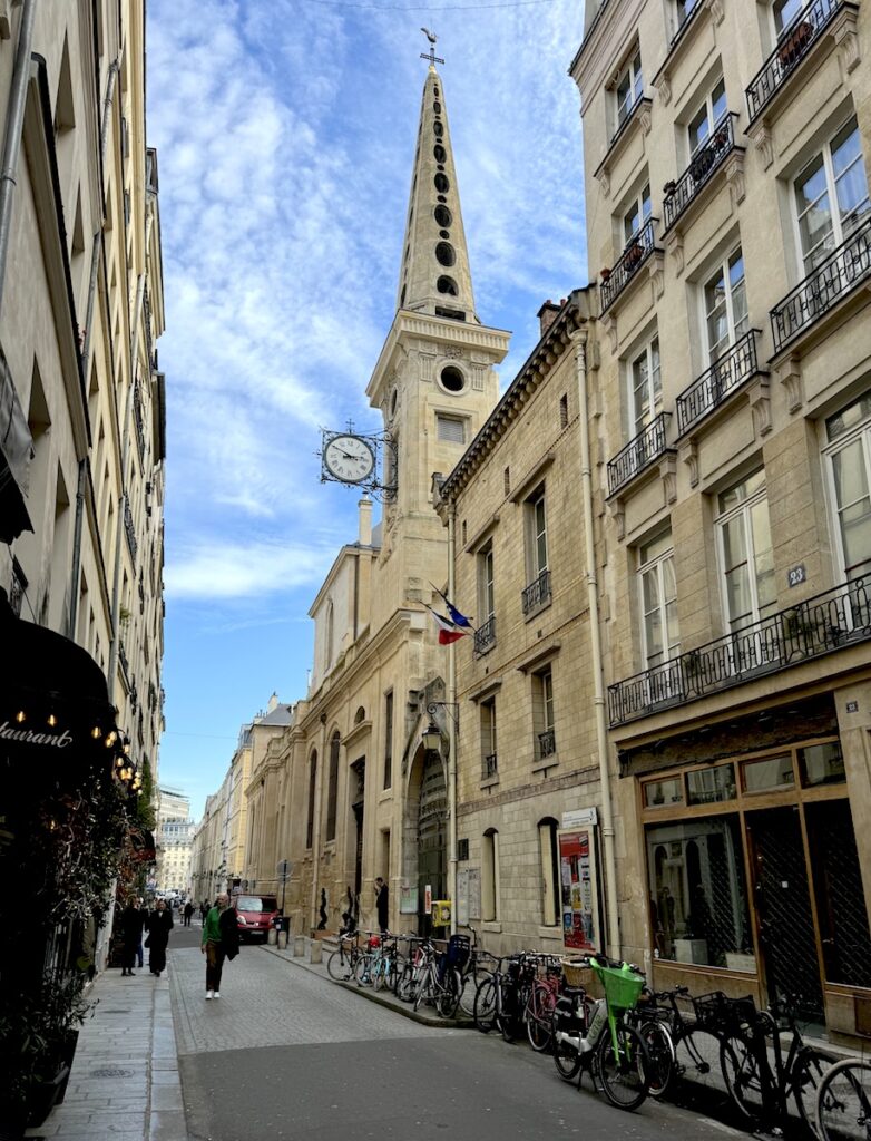 Narrow roadway lined with bikes and overlooking tall steepled church on sunny day. Ile Saint-Louis, Paris, France.