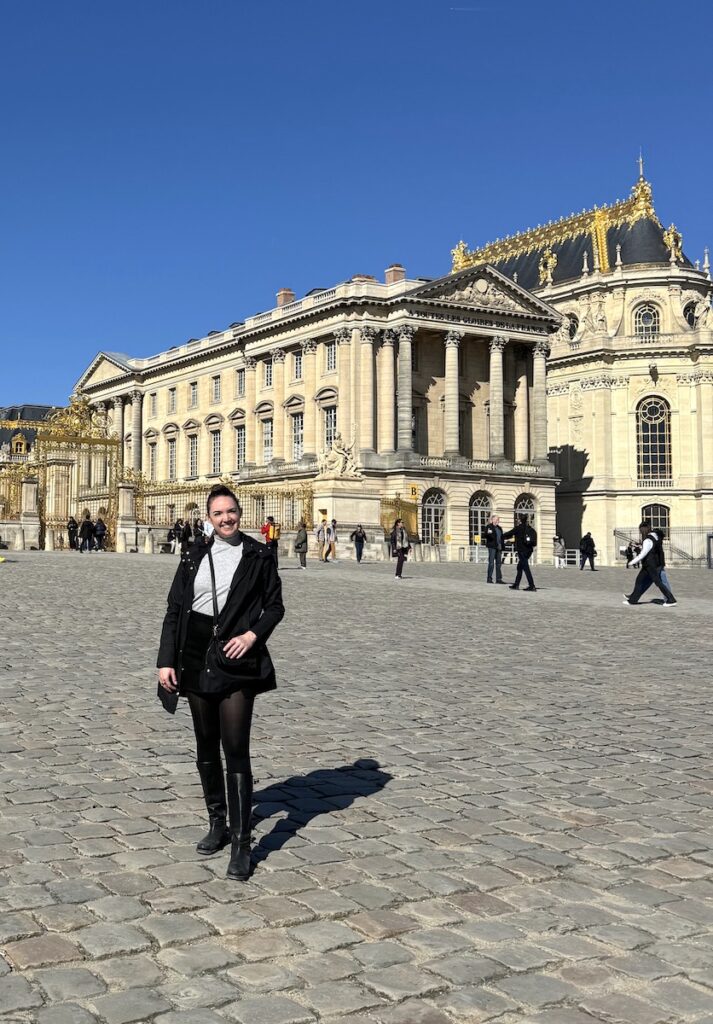 Woman in front of Palace of Versailles on sunny day. Palace of Versailles, France.
