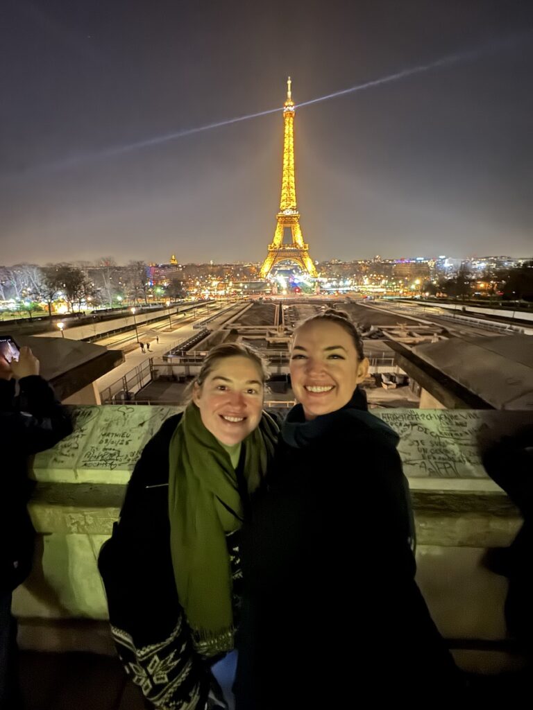 women in front of Eiffel Tower lit up at night from Tocadero Paris France