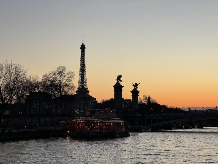 Silhouette of Eiffel Tower during sunset, view from the calm Seine River with boats in foreground. Sunset Happy Hour Cruise with Les Vedettes du Pont Neuf, Paris, France.