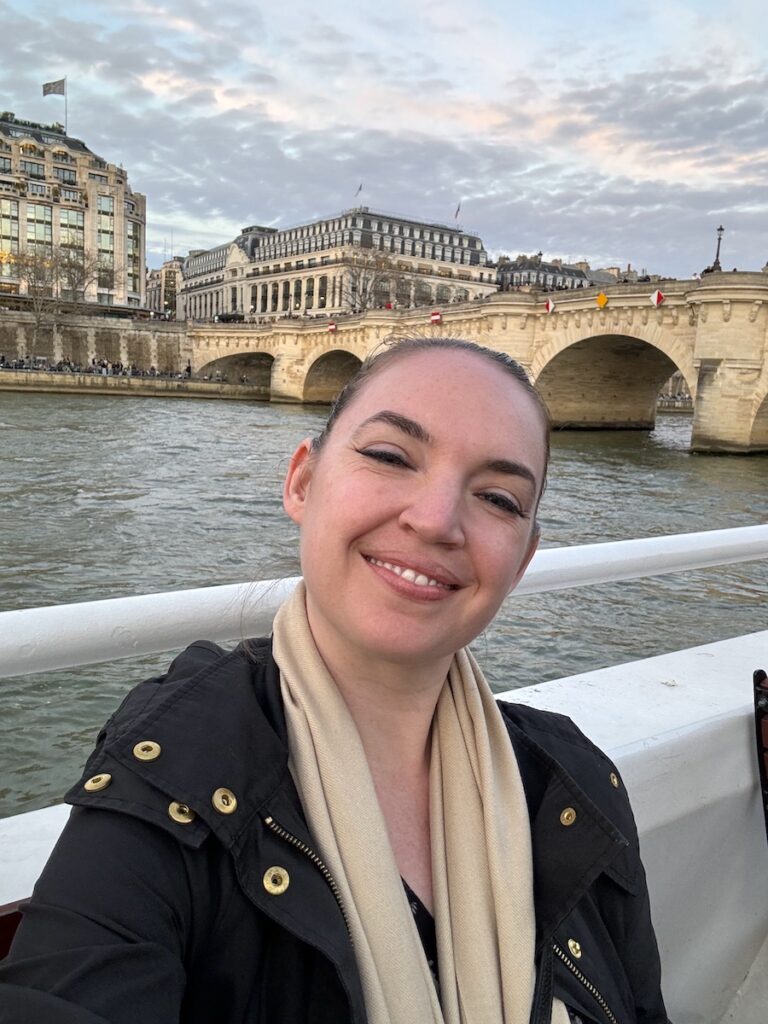 woman smiling on boat with historic bridge and buildings in background sunset happy hour cruise seine river paris france