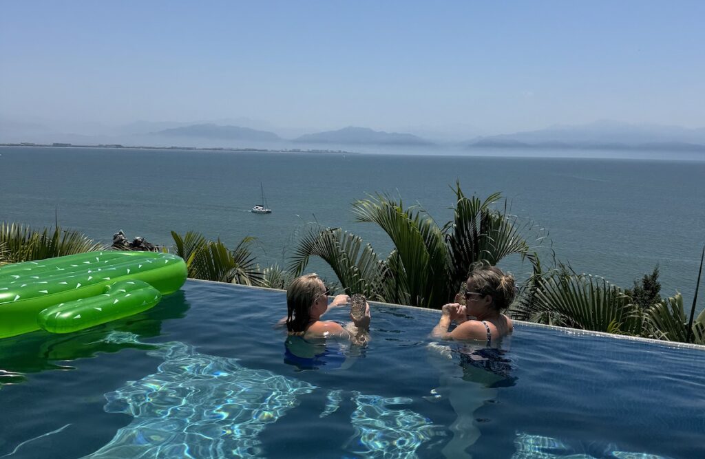 women in sunny infinity pool overlooking ocean near puerto vallarta and punta mita Mexico