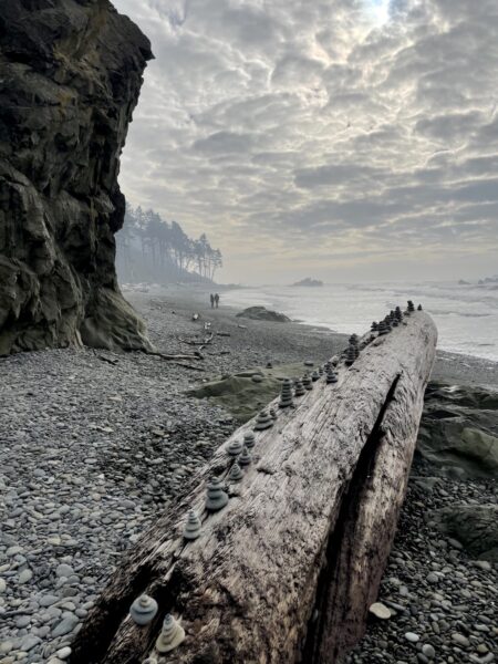 Silhouette of people walking on rocky beach with sea stacks rocky shore in background on hazy afternoon. Ruby Beach, Olympic National Park, Olympic Peninsula, Washington.