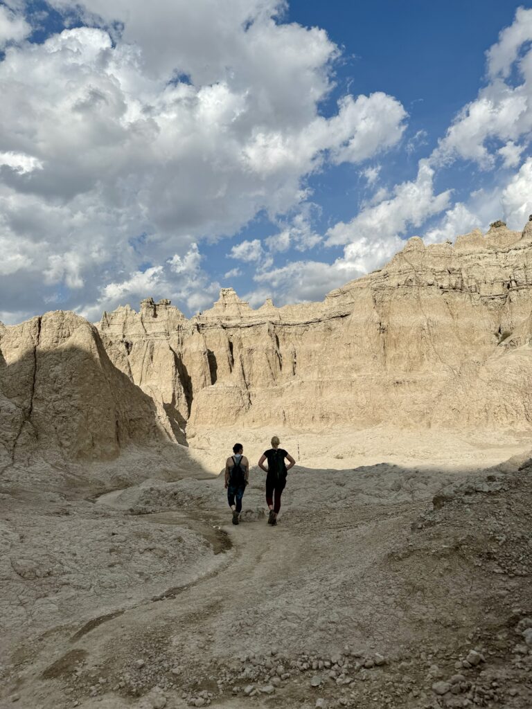 Two women hiking through tan colored badland canyon on sunny day. Notch Trail, Badlands National Park, South Dakota.