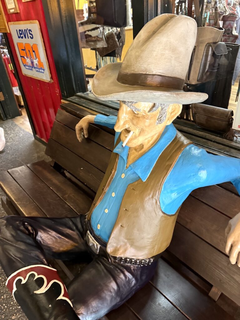 Statue of old cowboy sitting on bench in indoor mall, Wall Drug, Wall, South Dakota.
