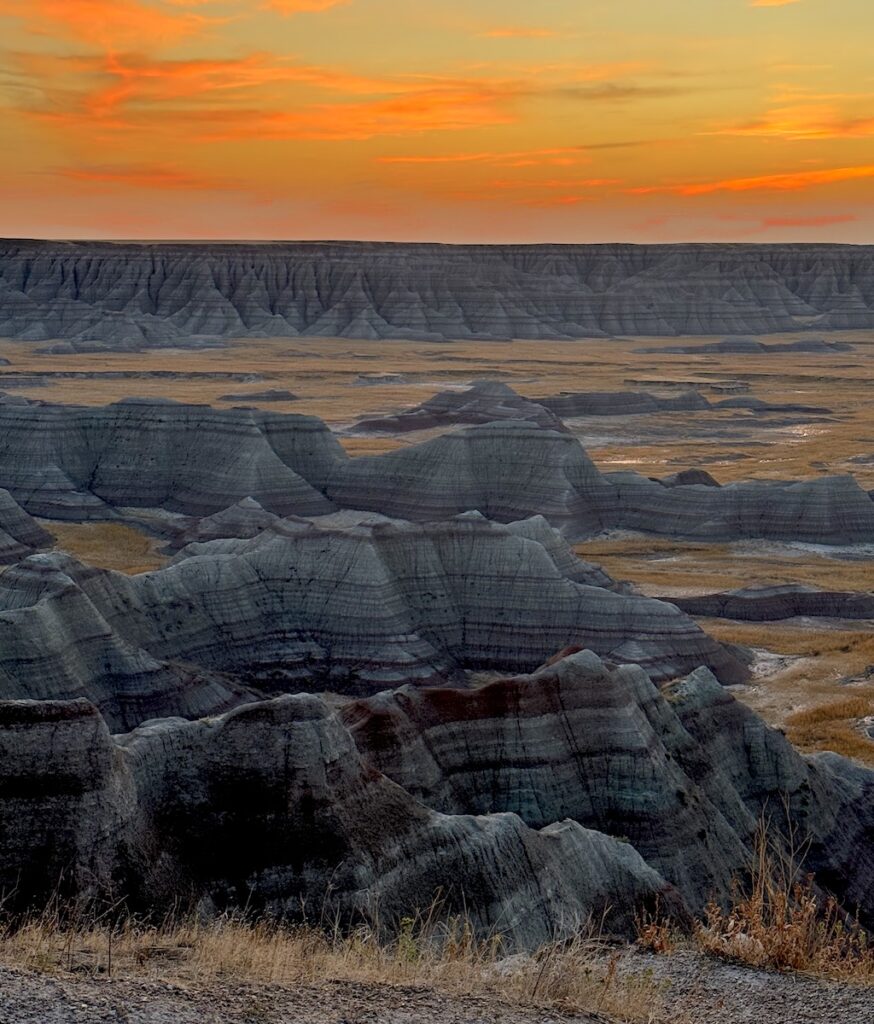 Bright orange sunrise over the colorful striped badlands in Badlands National Park, Big Badlands Overlook, South Dakota.