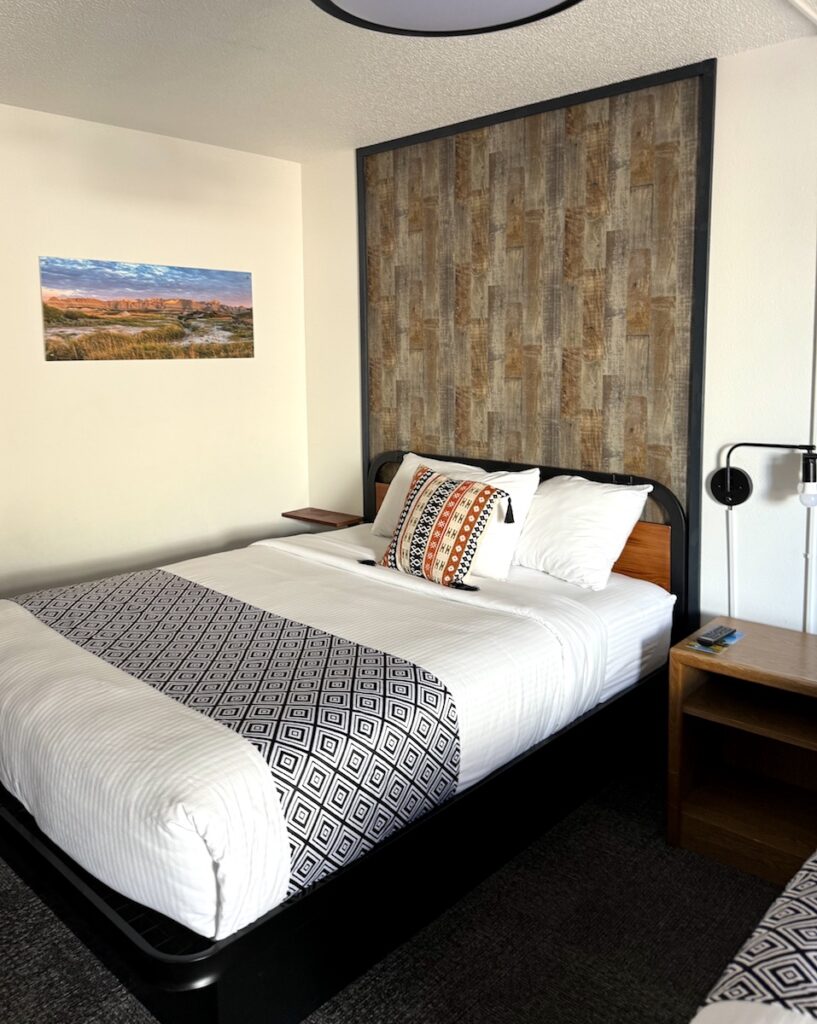 Guest bed with modern and updated bedding and rustic headboard. Hansen Inn & Cabins, Wall, South Dakota.