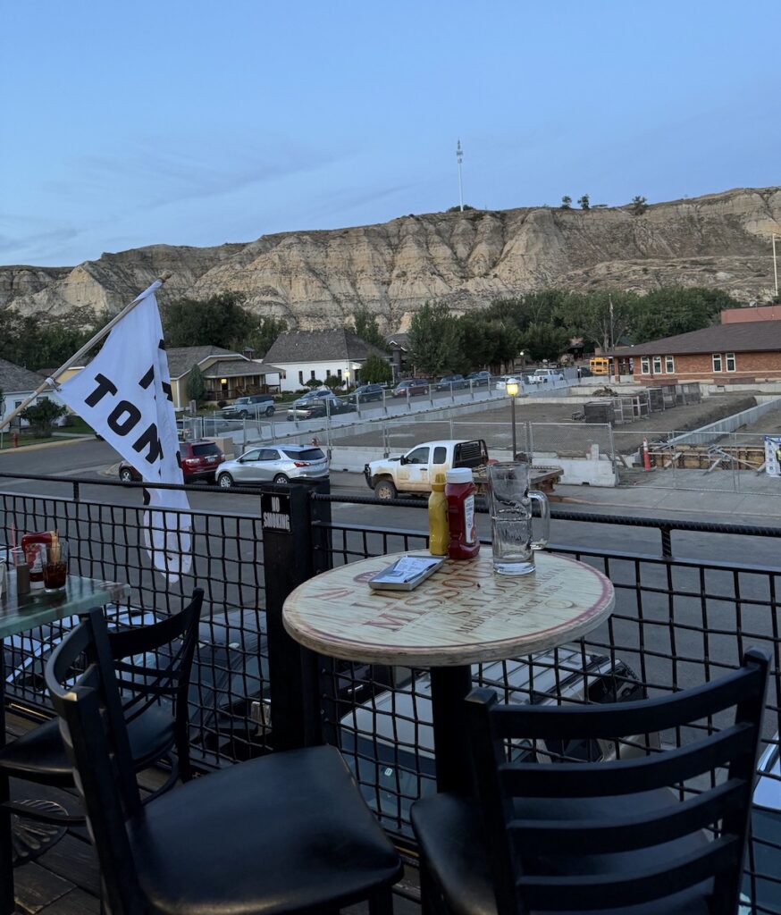 Small bistro table on outdoor rooftop deck at restaurant overlooking badlands during dusk. Little Missouri Saloon, Medora, North Dakota.
