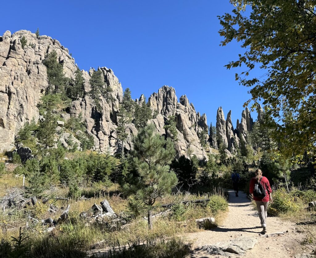 Woman hiking through rocky mountains with cathedral like spires on sunny fall day. Cathedral Spires Trail, Custer State Park, Black Hills, South Dakota.