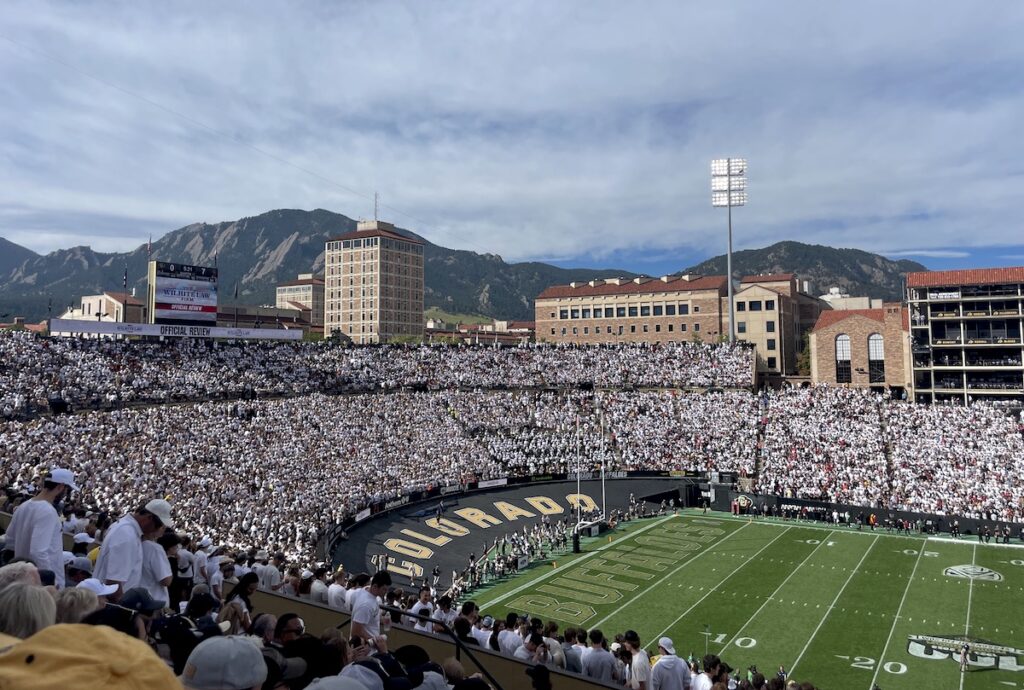 Football stadium full of fans in white with mountain views in background on sunny fall day. Folsom Field, University of Colorado, CU Football, Boulder, Colorado.