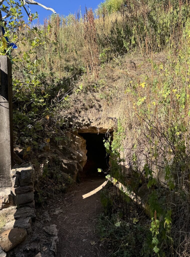 Small cave entrance in side of grassy hill on sunny day. Wind Cave National Park, Natural Cave Entrance, Black Hills, South Dakota.