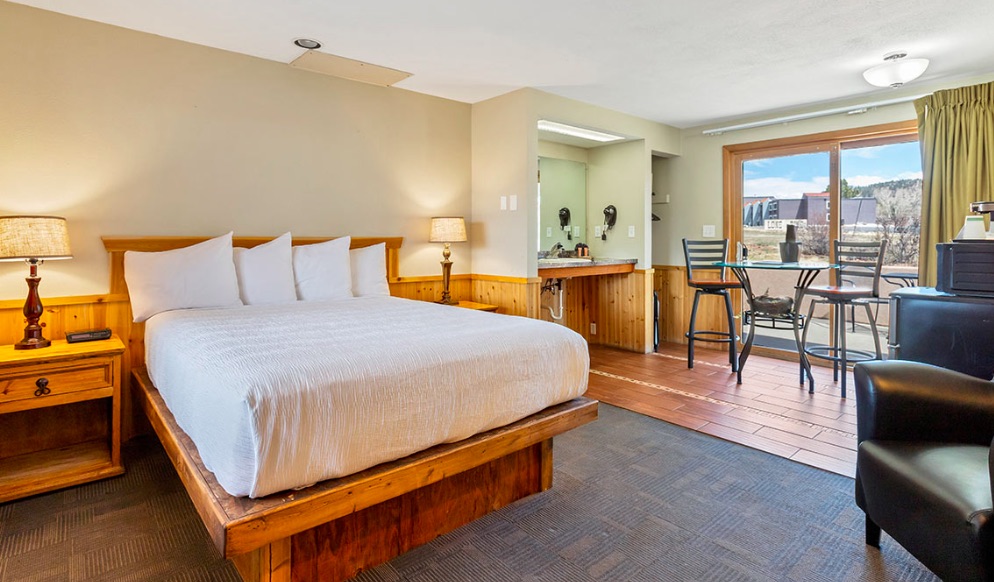 Guest room with queen size bed, small seating area and patio with mountain views. Guest room at Murphy's Resort at Estes Park, Estes Park, Colorado.