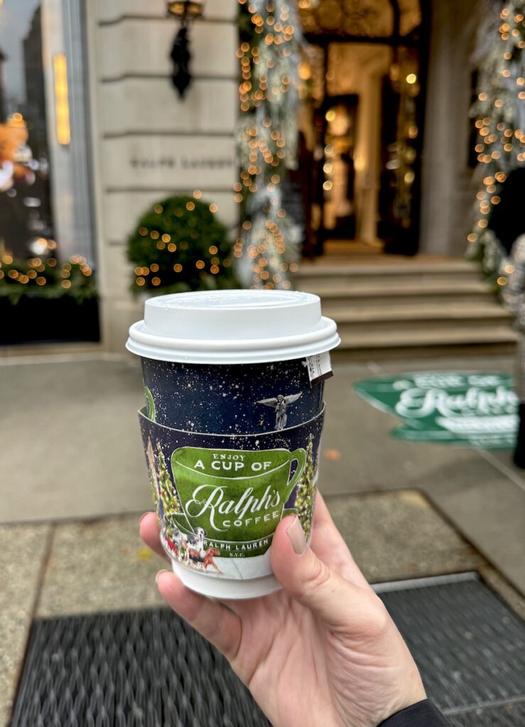 Woman holding colorful to-go coffee cup with starry night image on it and large green coffee mug reading "Enjoy a cup of Ralph's Coffee." Ralph's Coffee, Upper East Side, Manhattan, New York City, New York.