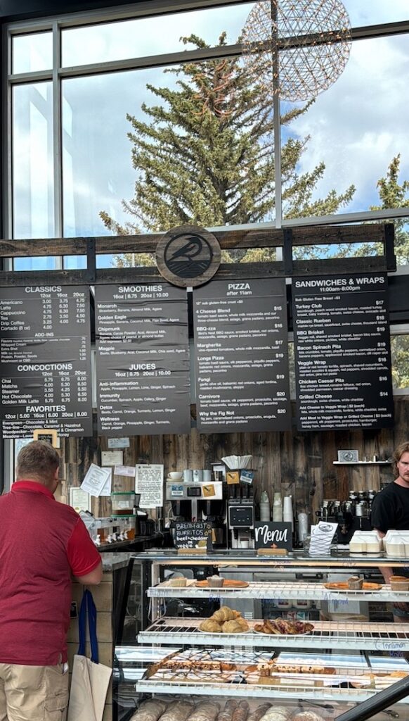 Guest and employee at coffee shop with huge multi-floor windows with mountain views in background. Bird's Nest Cafe, Estes Park, Colorado.