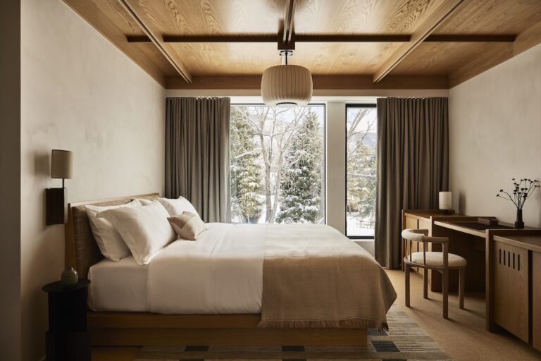 King size bed in luxury hotel room with modern, cozy decor with snow-covered trees outside. MOLLIE Aspen Hotel, Aspen, Colorado.