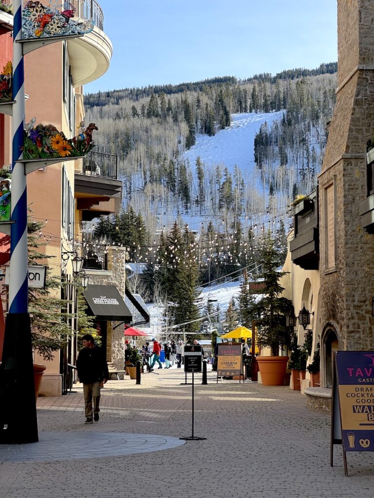Pedestrian walkway in luxury plaza directly under snow-covered ski resort on sunny winter day. Lionshead Village, Vail Mountain Resort, Vail, Colorado.