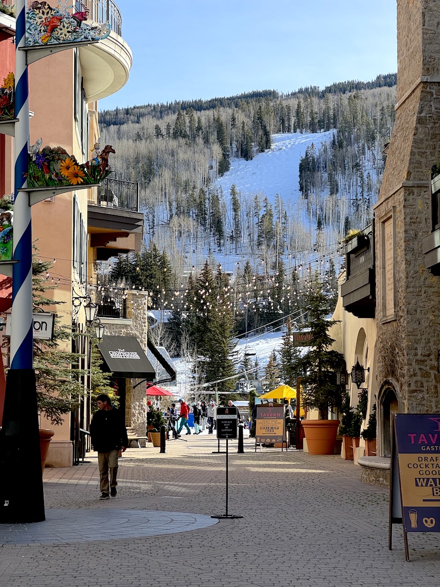 Pedestrian walkway in luxury plaza directly under snow-covered ski resort on sunny winter day. Lionshead Village, Vail Mountain Resort, Vail, Colorado.