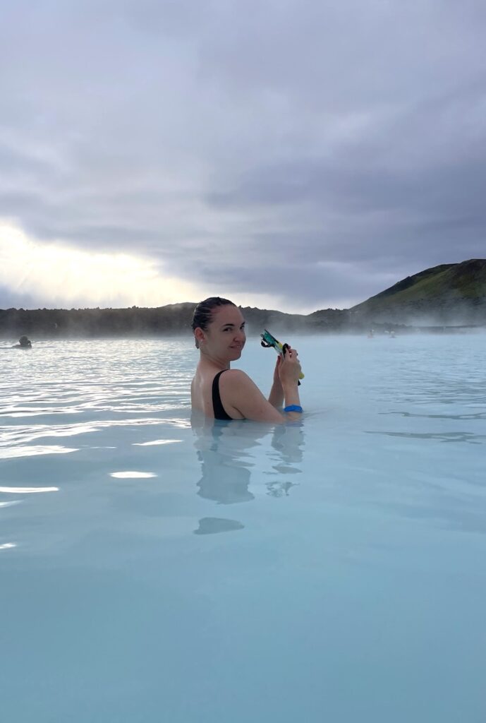 Woman smiling at camera while soaking in hot spring of bright blue water on gloomy morning. Blue Lagoon, Grindavík, Iceland.