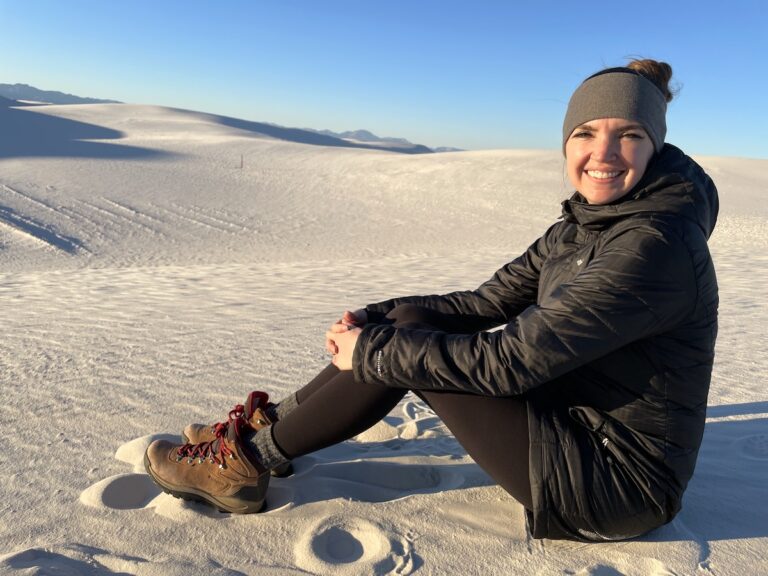 Woman sitting on sandy white dunes just before sunset on chilly evening in winter. Sunset from Alkali Flat Trail, White Sand Dunes National Park, New Mexico.