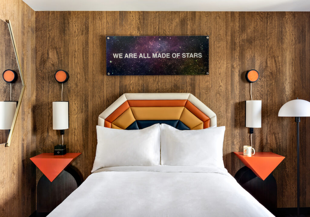 Retro style hotel room with funky and colorful headboards and night stands, wood paneled walls, and sign above bed reading "we are all made of stars." Americana Motor Hotel, Flagstaff, Arizona.