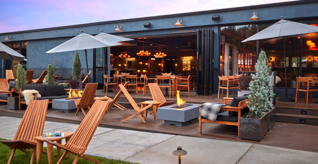 Large outdoor seating area of restaurant with wooden Adirondack chairs, fire pits, and umbrellas. High Country Motor Lodge, Flagstaff, Arizona.