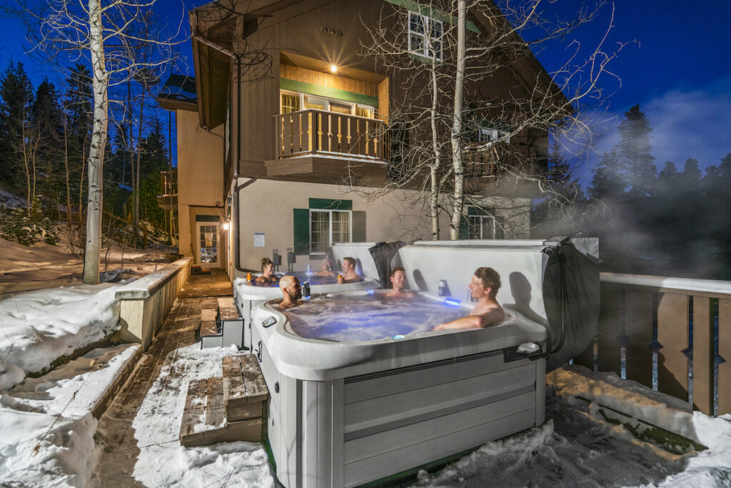 Hotel guests in two hot tubs outside mountain lodge hotel surrounded by snow and pine trees. Breckenridge Boutique Hotel, Breckenridge, Colorado.