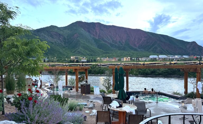 Couple sitting in riverside hot spring pool overlooking Colorado River and mountains at luxury hot spring resort in summer. Iron Mountain Hot Springs, Glenwood Springs, Colorado.