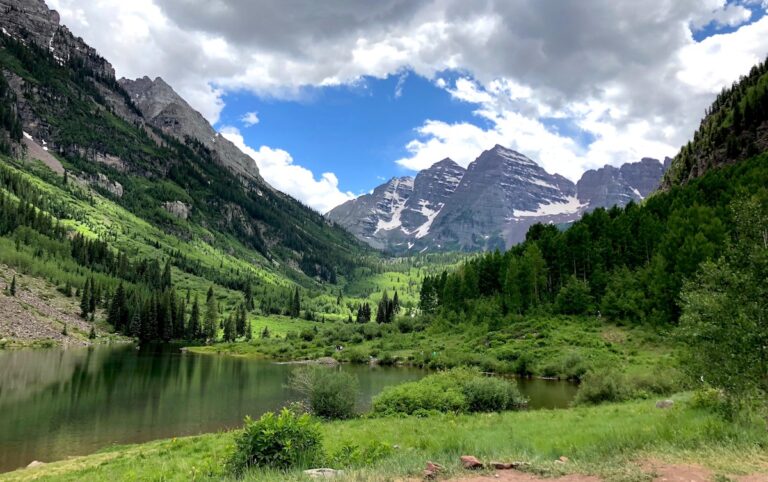 Jagged, snow-striped rocky peaks jutting up from lush green forest during summer. Maroon Bells, Aspen, Colorado.