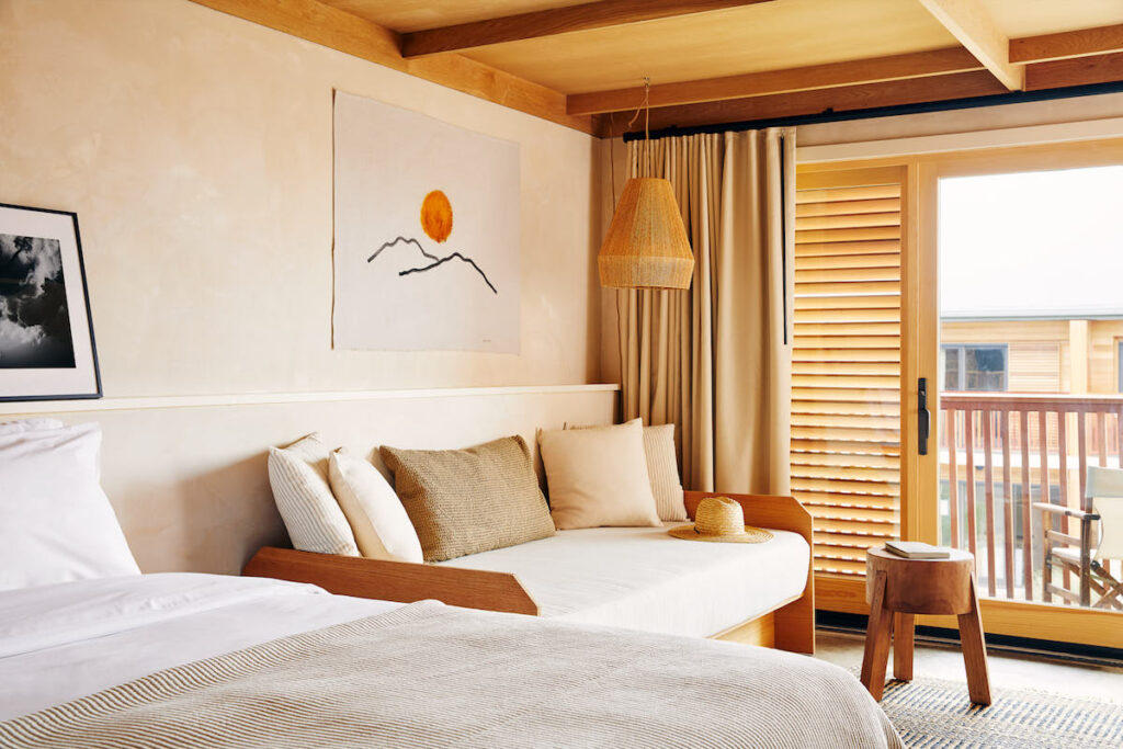 Luxury guest hotel room with cozy bed, seating area, patio, and upscale bohemian beach decor. Marram hotel, Montauk, New York, The Hamptons.