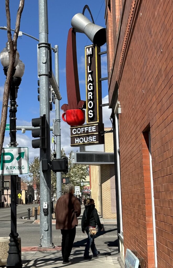 People walking through historic downtown area under large retro-style sign reading "Milagros Coffee House" Alamosa, Colorado.