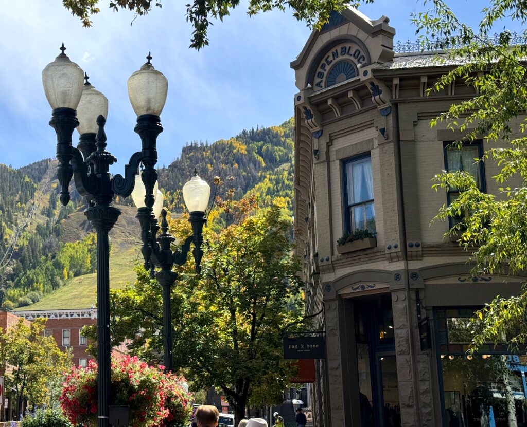 Historic building in mountain town framed by green lush trees and antique street lights on sunny fall day. Downtown Aspen, Colorado.