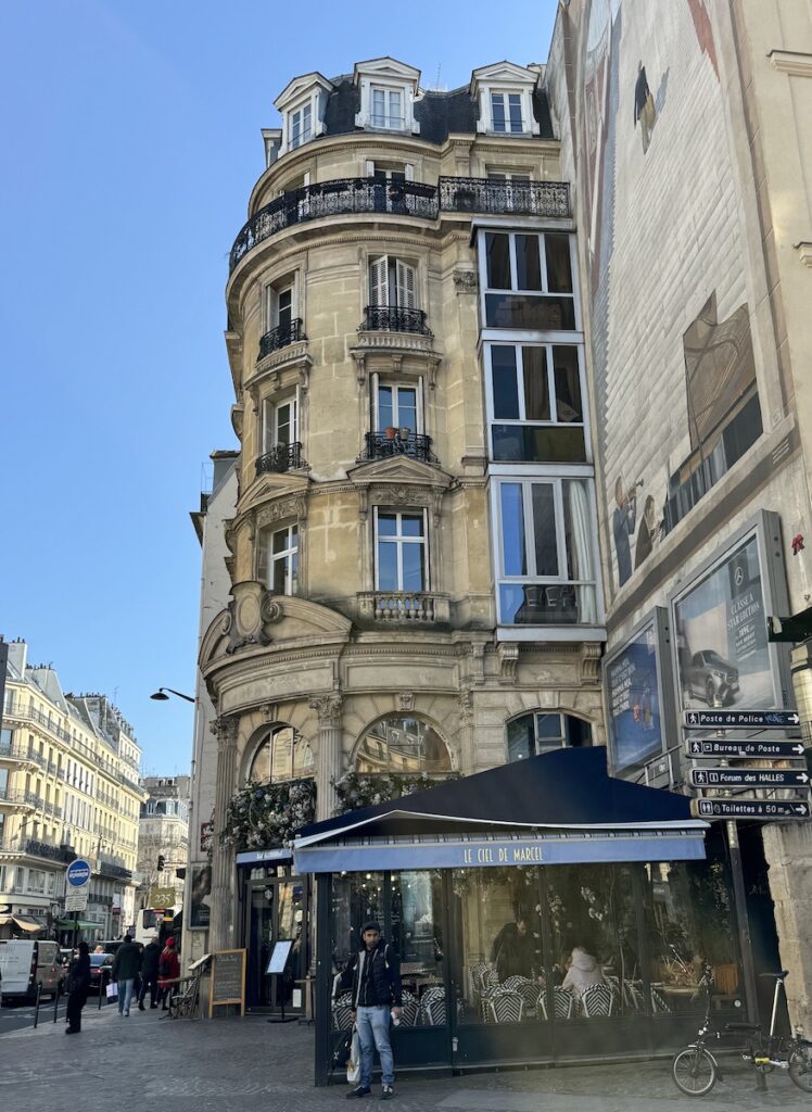 Ornate historic building and street with cafes and pedestrians. Narrow streets surrounded by historic buildings. Le Marais, 3rd Arr., Paris, France.