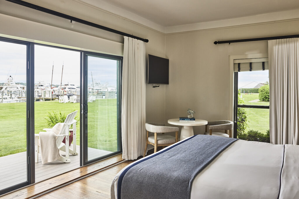 Luxury hotel guest room with bed overlooking marina and patio with outdoor seating. Montauk Yacht Club resort, Montauk, New York, The Hamptons.