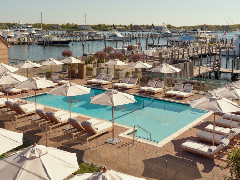 Outdoor pool surrounded by umbrellas and lounge chairs overlooking marina full of luxury boats and yachts on sunny summer day. Montauk Yacht Club resort, Montauk, New York, The Hamptons.