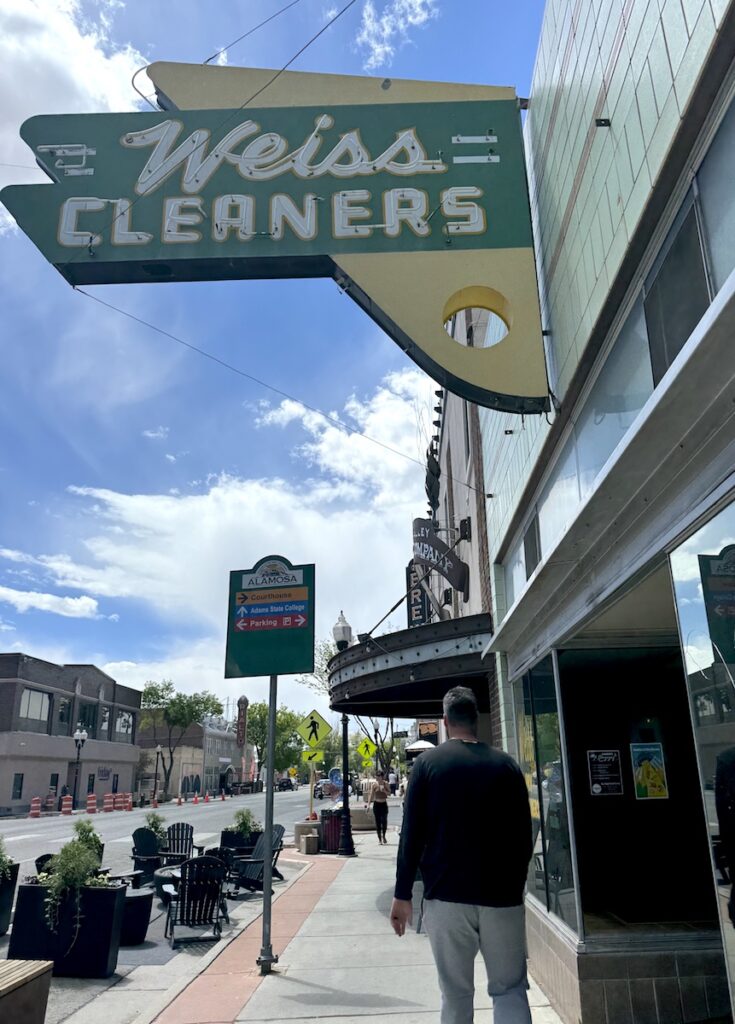 Retro neon sign reading "Weiss Cleaners" in historic downtown area on sunny summer day. Alamosa, Colorado.