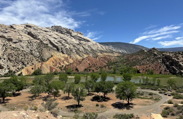 Calm green river flowing alongside huge orange and white rock cliffs on sunny summer day. Split Mountain Campground, Dinosaur National Monument, Utah.