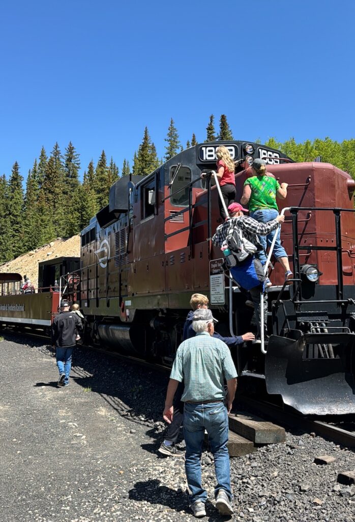 People climbing into historic train engine in the mountains on a sunny summer day. Leadville Railroad, Leadville, Colorado.