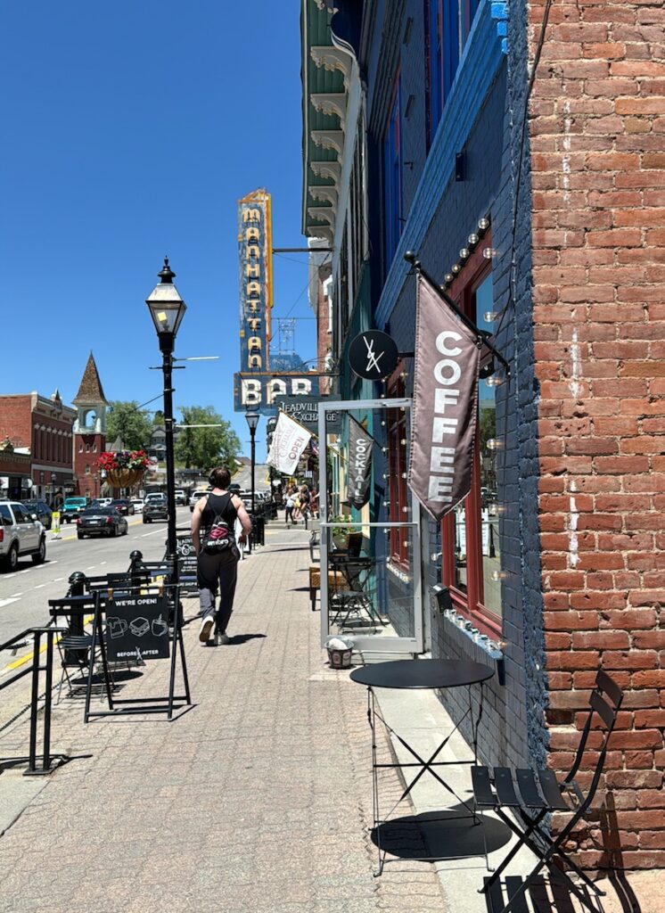 People walking along downtown area lined with brick buildings and old historic neon signs on sunny summer day. Historic downtown Leadville, Colorado.