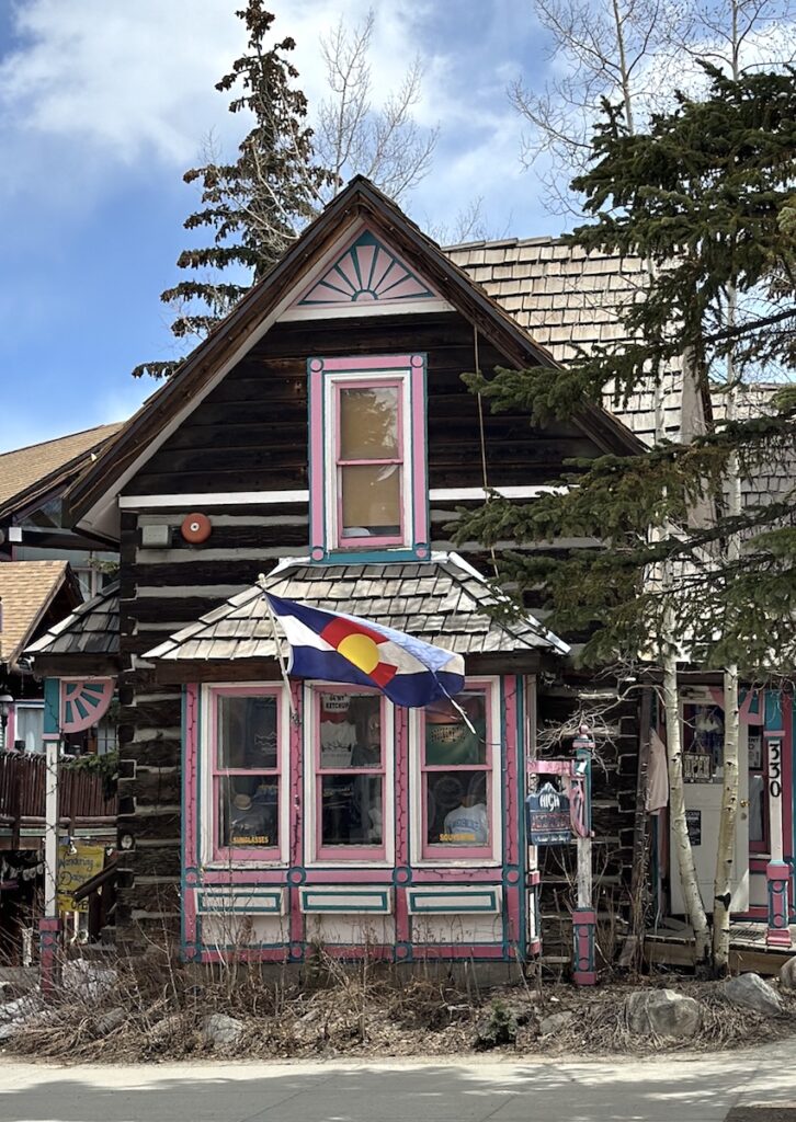 Historic log house with colorful pink and blue trim and Colorado state flag on sunny summer day. Historic downtown Breckenridge, Colorado.